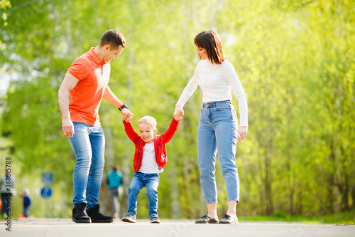 Happy Caucasian family parents and kid boy on outdoor park, sunlight. Hold hands