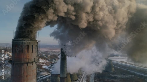 Drone around toxic enterprise chimneys tubing against the sky background release black smoke. Factory pollutes environment. Russia Primorsky Krai industrial countryside landscape. Winter day. Aerial photo