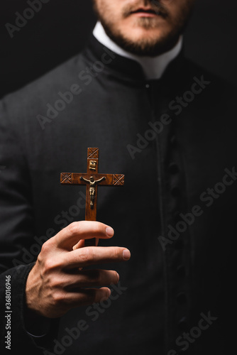 selective focus of priest holding wooden cross isolated on black
