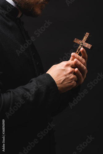 cropped view of priest holding wooden cross isolated on black