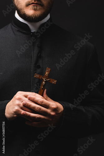 Canvas Print cropped view of bearded priest holding wooden cross isolated on black