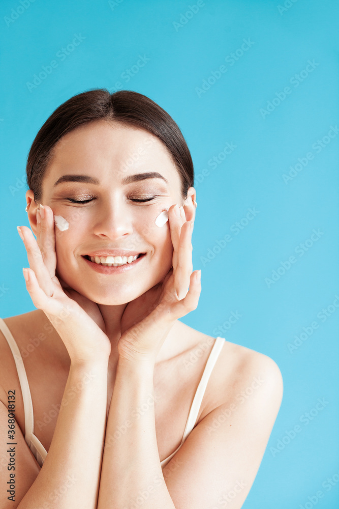 Lovely young woman with healthy skin is applying a cream on her face Lovely young woman with healthy skin is applying a cream on her face