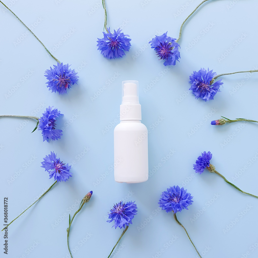 Top view and close-up of mockup of unbranded white plastic spray bottle and floral frame of blue lowers on a pastel blue background. Natural organic spa cosmetics and liquid antimicrobial spray. Top view and close-up of mockup of unbranded white plastic spray bottle and floral frame of blue lowers on a pastel blue background. Natural organic spa cosmetics and liquid antimicrobial spray.