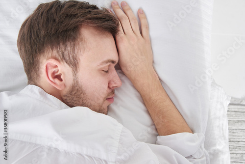 Close-up portrait of sleeping brunette man on white pillow