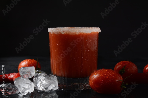 A glass with a cocktail "Bloody Merry" with ice on a black background, the top of the glass is decorated with salt