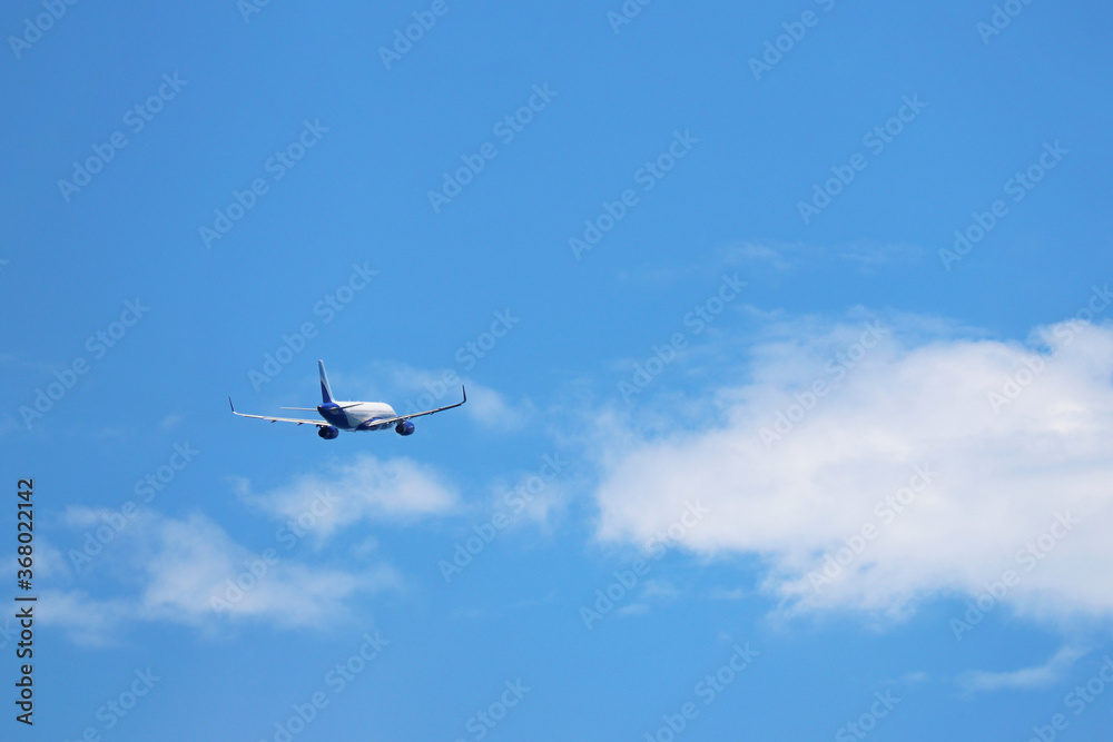 Airplane flying in the blue sky on background of white clouds, rear view. Twin-engine commercial plane during the turn, vacation and travel concept Airplane flying in the blue sky on background of white clouds, rear view. Twin-engine commercial plane during the turn, vacation and travel concept