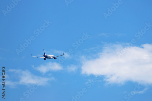 Airplane flying in the blue sky on background of white clouds, rear view. Twin-engine commercial plane during the turn, vacation and travel concept