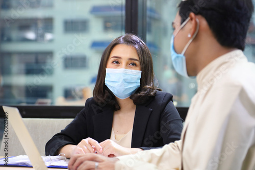 Business women in formal wear with protective facial mask discussing with colleague in business office following new normal and social distancing policy during covid-19 or coranavirus pandemic photo