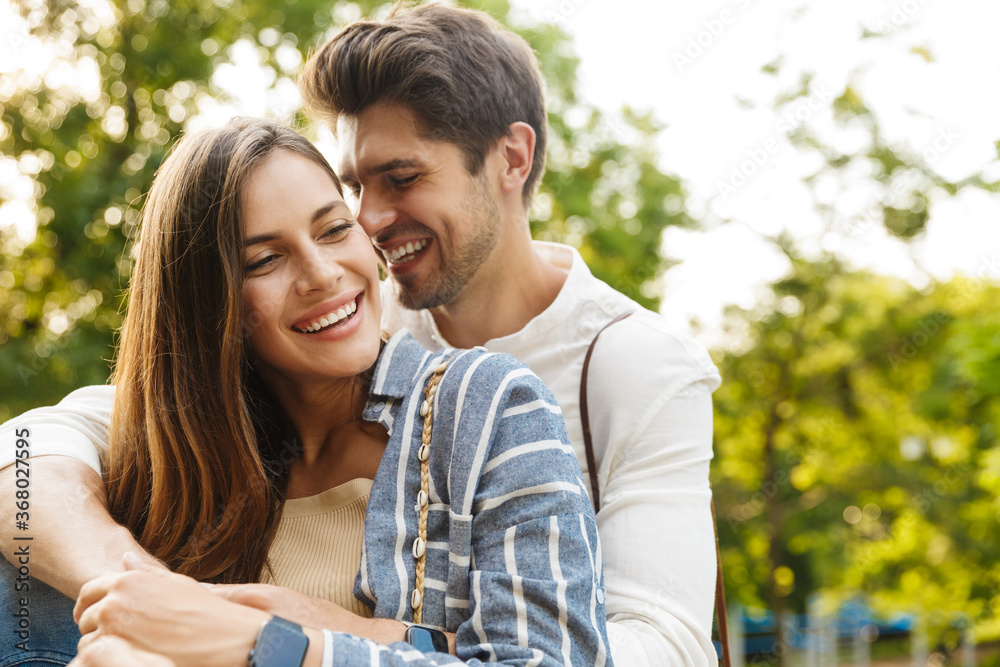 Image of caucasian couple smiling and hugging while walking in park Image of caucasian couple smiling and hugging while walking in park