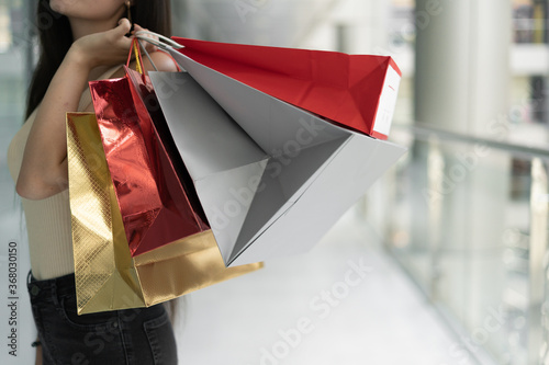 Close-up of shopping bags in a woman's hand, advertising shopping in a fashion store, female hand holds red and white packages. Shopping center.