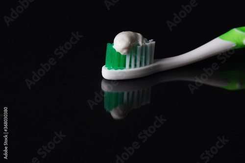 Toothbrush with toothpaste on black background with reflection