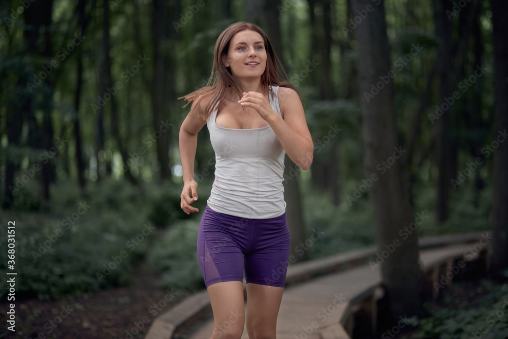 Happy brunette girl in shorts and a tank top runs in a summer park. Happy brunette girl in shorts and a tank top runs in a summer park.