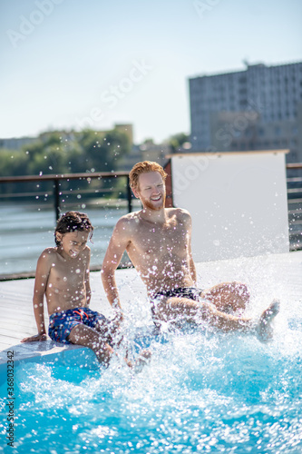 Fotografie Cheerful dad with son making splashes in pool