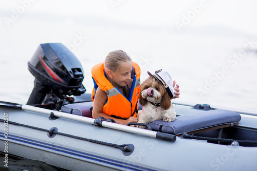 Little girl in a life jacket with her dog in a boat on the lake. Safety. summer rest.