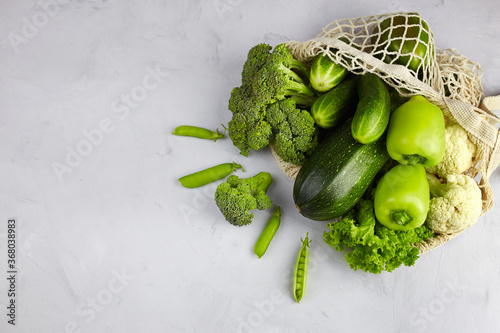 Green vegetables in  string bag on light background. Zucchini, cucumber, pepper, broccoli, cauliflower, green peas. No plastic, zero waste.