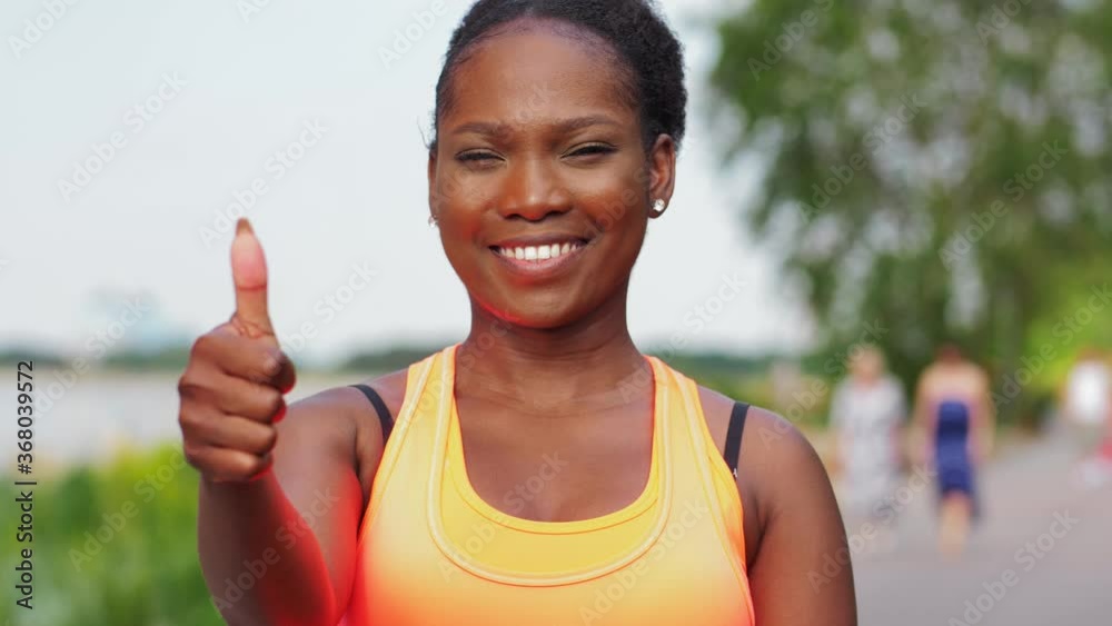 fitness, sport and healthy lifestyle concept - happy smiling young african american woman in sports clothes showing thumbs up outdoors fitness, sport and healthy lifestyle concept - happy smiling young african american woman in sports clothes showing thumbs up outdoors