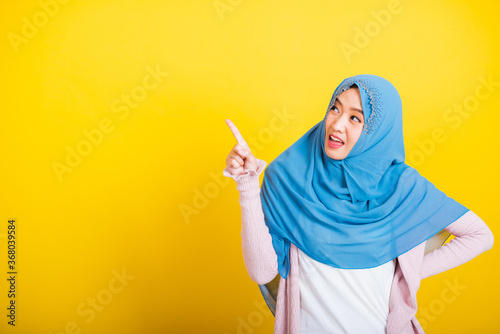Asian Muslim Arab, Portrait of happy beautiful young woman Islam religious wear veil hijab funny smile she positive expression pointing finger side sideways to space isolated yellow background © sorapop