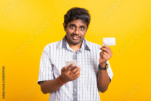 Closeup Asian happy portrait young black man holds a mobile smartphone and showing credit card for mobile payment shopping online concept, studio isolated on yellow background