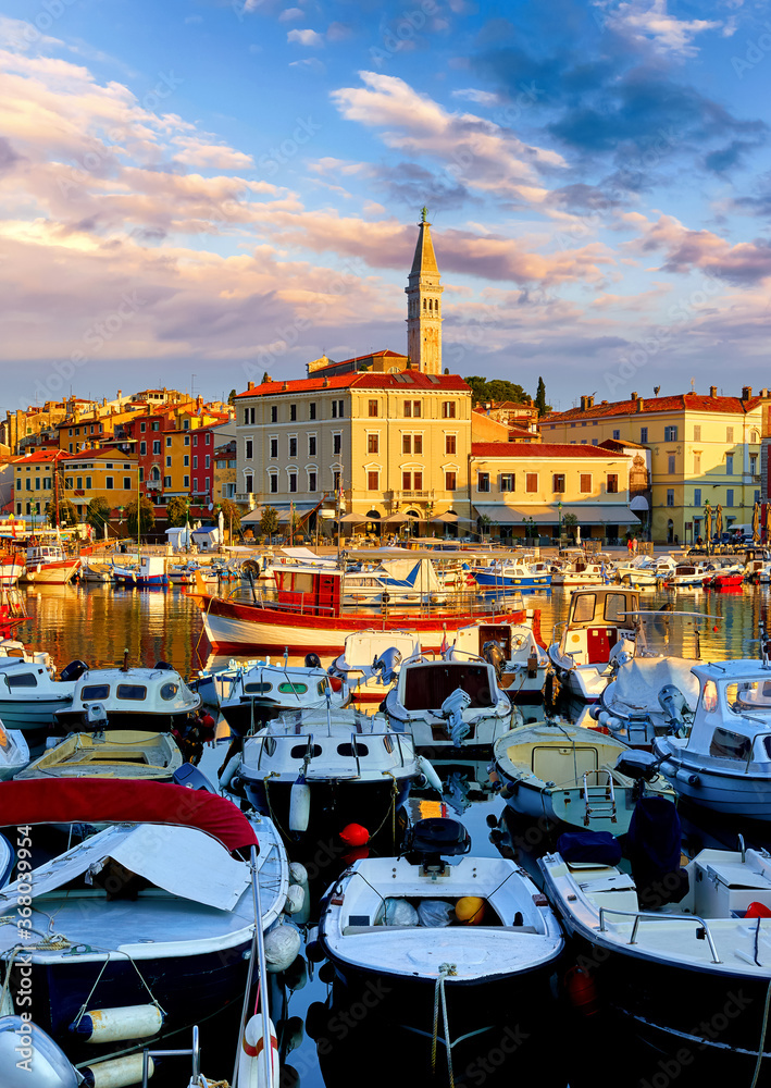 Rovinj, Istria, Croatia. Motorboats and boats on water in port Rovigno. Medieval vintage houses of old town. Yachts landing, high tower of Church of Saint Euphemia. Morning sunrise blue sky withclouds