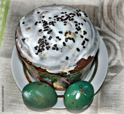 Traditional sugar-topped Easter cake with colored Easter eggs on the linen tablecloth. Table decoration. Spring holidays. Closeup