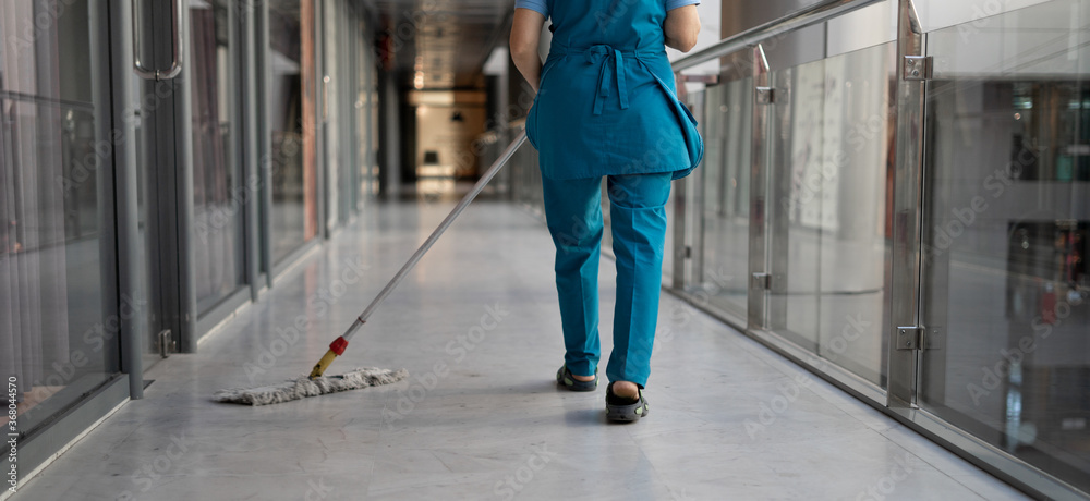 Close-up of a woman's legs in a blue work uniform. Mopping the mall floor with a mop. Wet cleaning of the room. Copy space