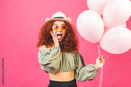 Happy holiday! Happy young curly smiling woman with balloons isolated over pink background. Valentines day or womans day.