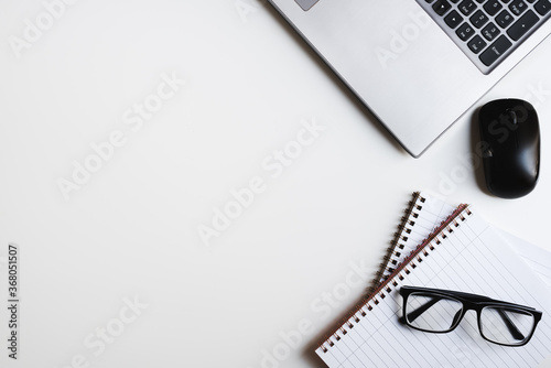 Laptop keyboard, computer mouse, notebooks and reading glasses on white office table, top view. Freelance flat lay
