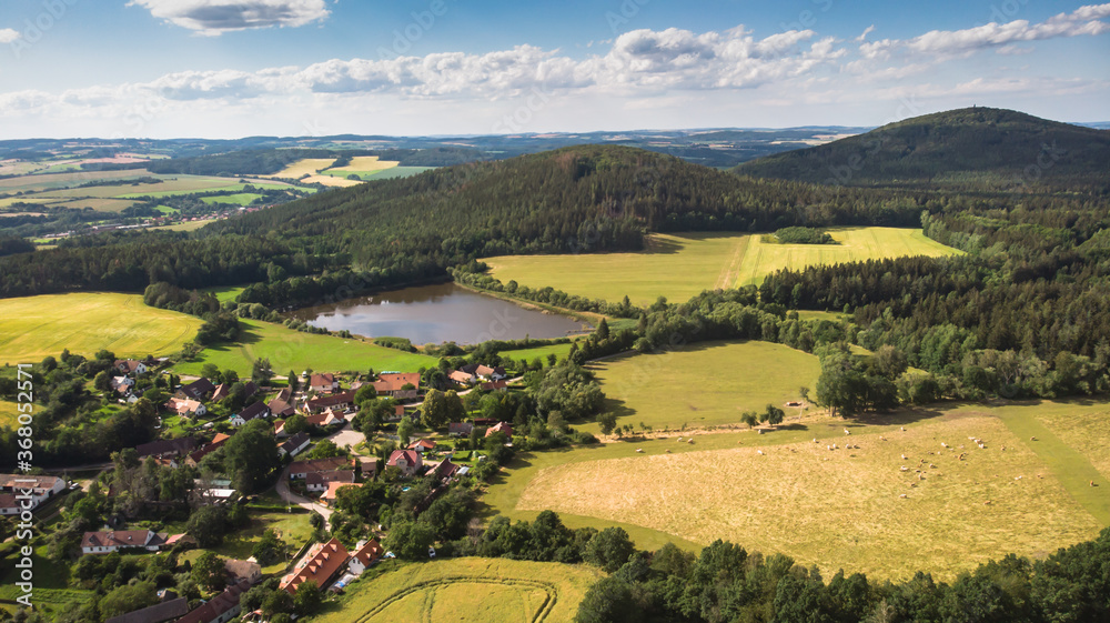 Aerial view of idyllic hilly landscape and small village.Houses from above, real estate concept.Natural summer scenic countryside. Beautiful view of green valley,meadows and lake in the Czech republic
