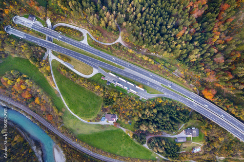 Top dawn aerial view of freeway speed road between yellow autumn forest trees and blue river.