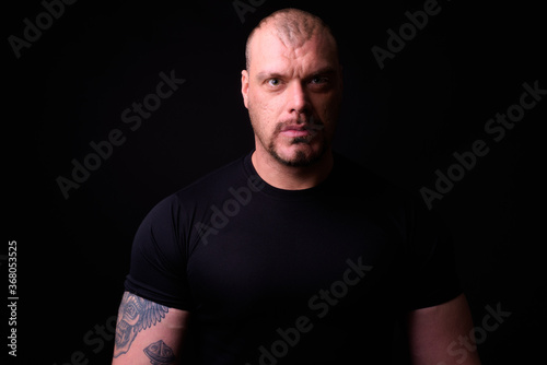 Portrait of muscular bald man against black background