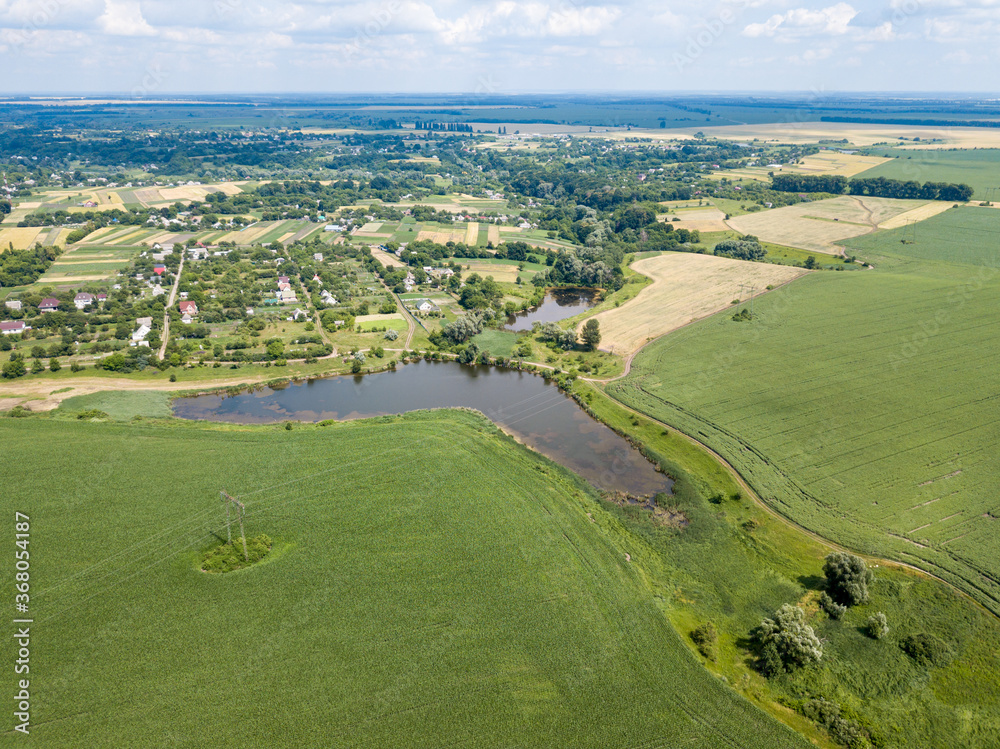 Obraz premium Aerial drone view. A field of ripening wheat and corn in Ukraine near the lake.