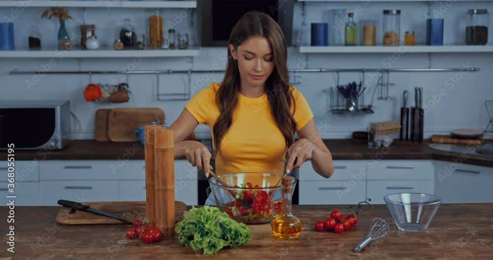 happy woman mixing fresh salad in kitchen