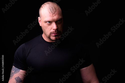 Portrait of muscular bald man against black background © Ranta Images