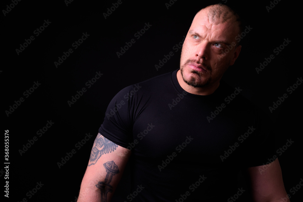 Portrait of muscular bald man against black background