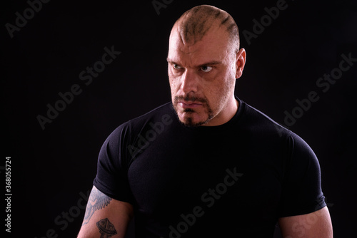 Face of muscular bald bearded man against black background © Ranta Images