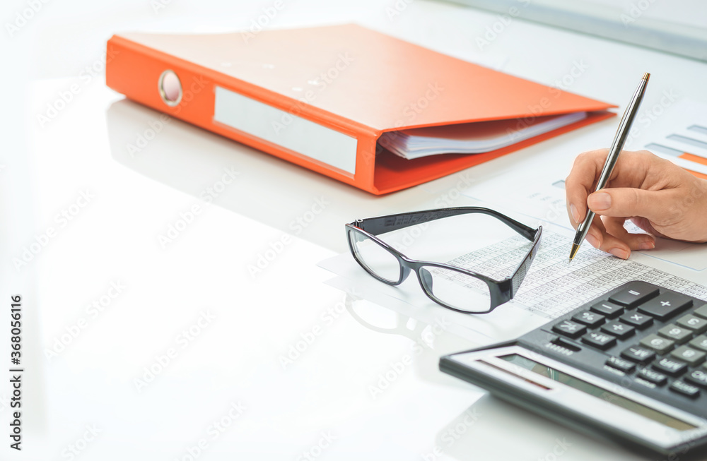 Finance and business. Financial office space with graphs. Paperwork binder and calculator, hand of a person working at desk with stats data. Cost revenue salary or small business. Copy space Finance and business. Financial office space with graphs. Paperwork binder and calculator, hand of a person working at desk with stats data. Cost revenue salary or small business. Copy space
