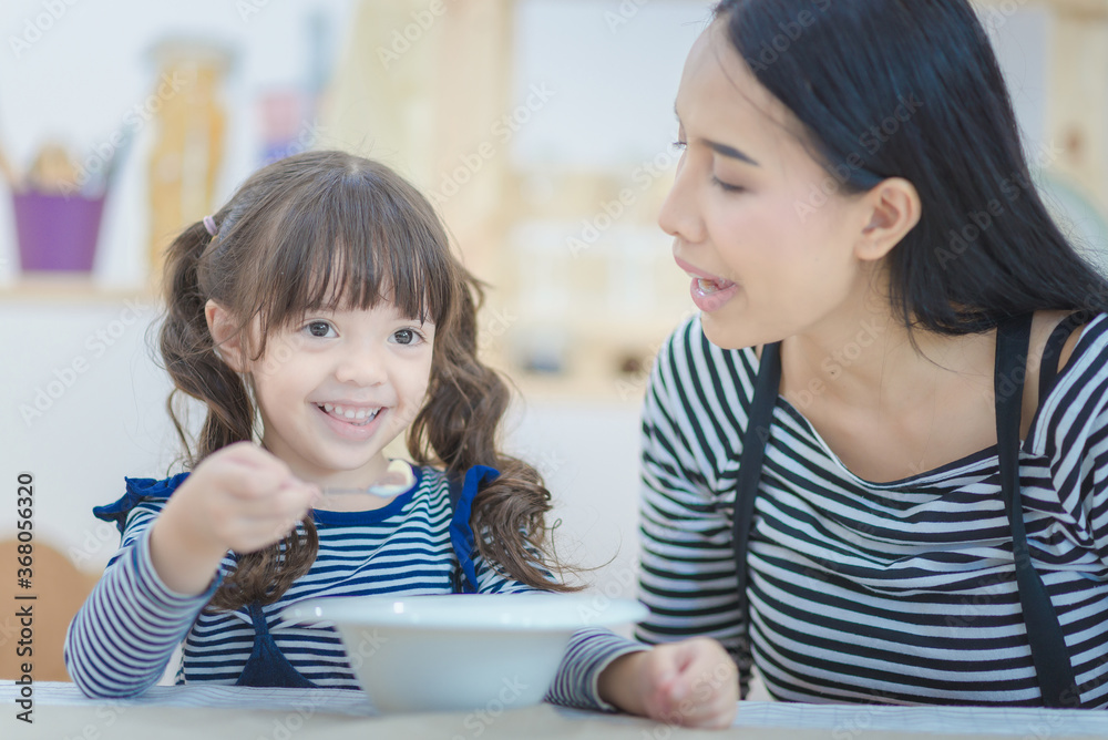 Happy family of asian mom feeding healthy breakfast to her cute daughter in the morning. Photo series of family, kids and happy people concept. Happy family of asian mom feeding healthy breakfast to her cute daughter in the morning. Photo series of family, kids and happy people concept.