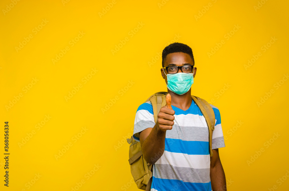 closeup of a young handsome african man wearing face mask to prevent, prevented, preventing himself from the outbreak in the society and did thumbs up