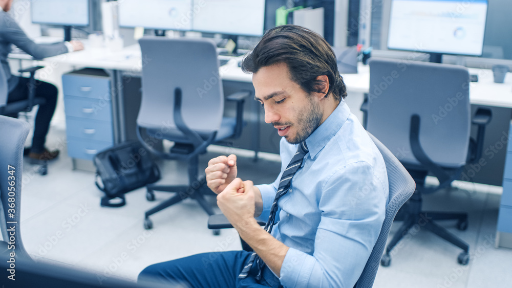 Handsome Tie Wearing Office Worker Uses Desktop Computer, Achieves Great Results, Cheerfully Celebrates His Success with YES Gesture. Confident Young Businessman Works in the Big Bright Office. Handsome Tie Wearing Office Worker Uses Desktop Computer, Achieves Great Results, Cheerfully Celebrates His Success with YES Gesture. Confident Young Businessman Works in the Big Bright Office.