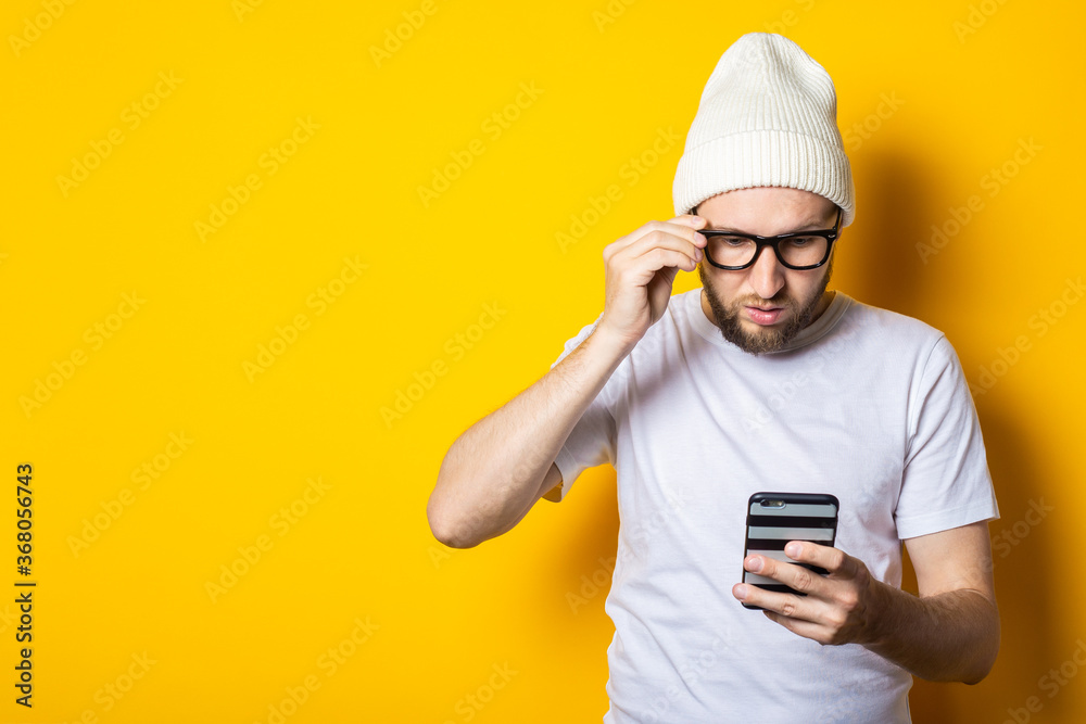 Bearded young man looks at the phone with concentration on a yellow background. Bearded young man looks at the phone with concentration on a yellow background.