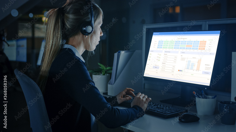 Working Late at Night in the Office: Businesswoman Using Desktop Computer, Using Headsets and Making Calls, Talking to Clients and Customers, Analyzing, Solving Problems. Working Late at Night in the Office: Businesswoman Using Desktop Computer, Using Headsets and Making Calls, Talking to Clients and Customers, Analyzing, Solving Problems.