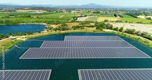 Solar panles park floating in a blue pond. We can see the panels floating on water with countryside in the background - aerial view 4K photo
