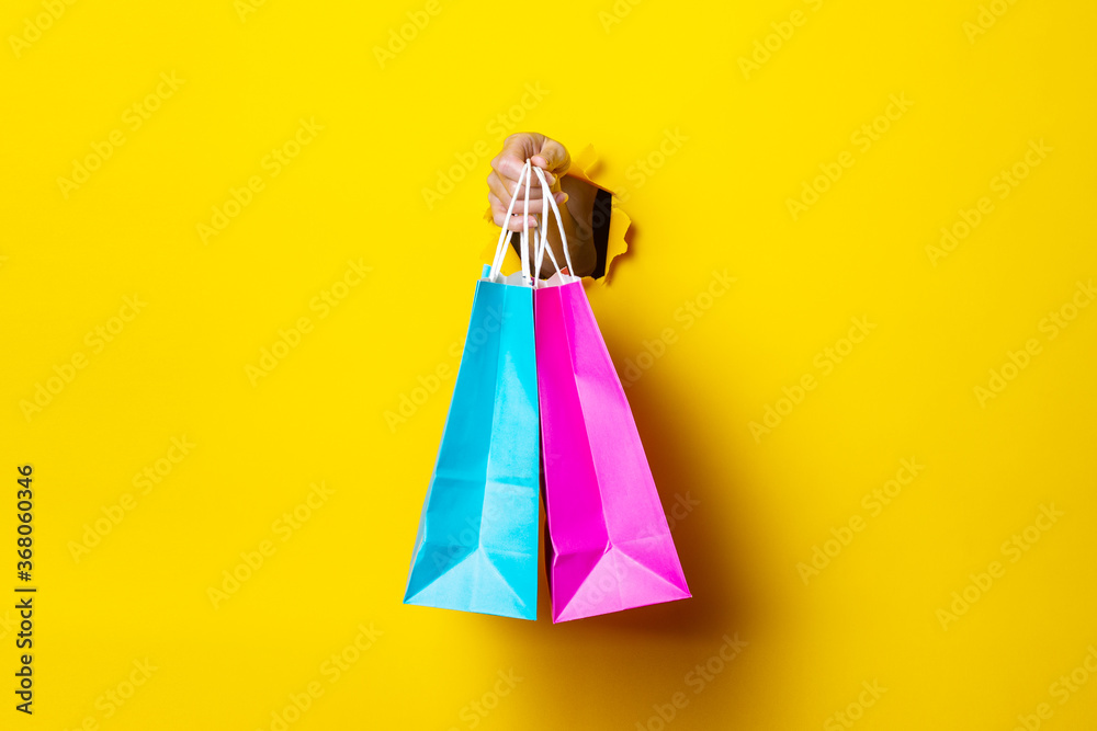 Female hand holds a pink and blue shopping bag on a yellow background