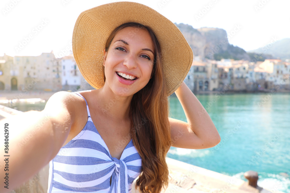 Smiling woman take selfie in her summer vacation in Cefalu, Mediterranean Sea, Italy