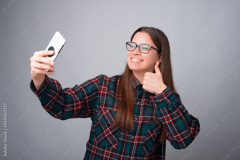 Young lady is making a selfie with her phone over grey background.