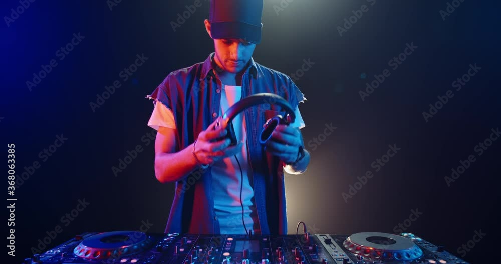 A cool young dj approaches the mixer controller and puts headphones on, ready to perform in a nightclub - nightlife concept 4k footage