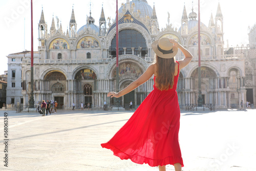 Holidays in Venice. Back view of pretty girl in elegant red dress dancing in St Mark's Square in Venice, Italy. Beautiful young woman visiting Europe.