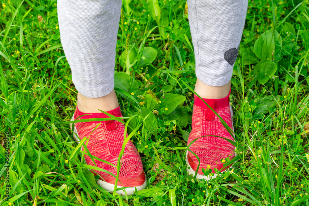 legs young girl dress  gray pants and red sports sneakers stand  green grass on sunny day