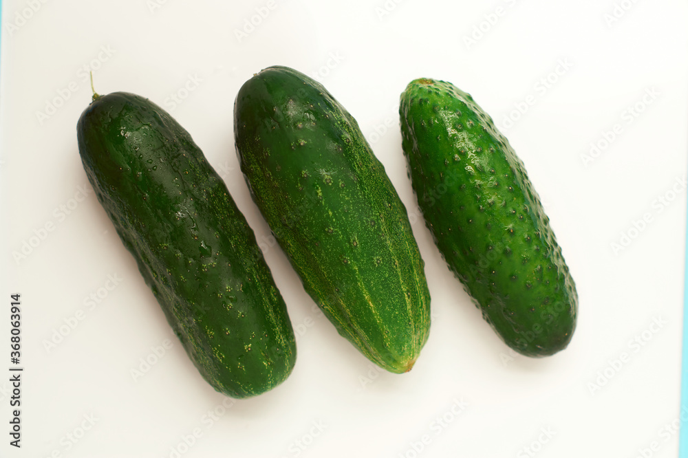 Three green cucumbers of different shapes on a white background. Three green cucumbers of different shapes on a white background.