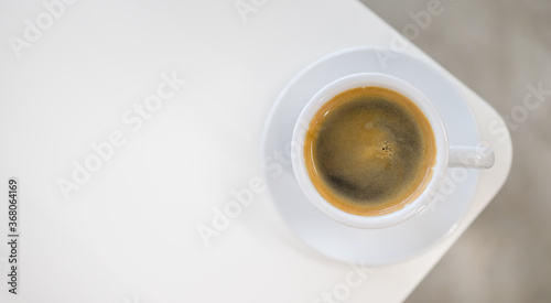Top view of white cup of hot black coffee and crema on white table .